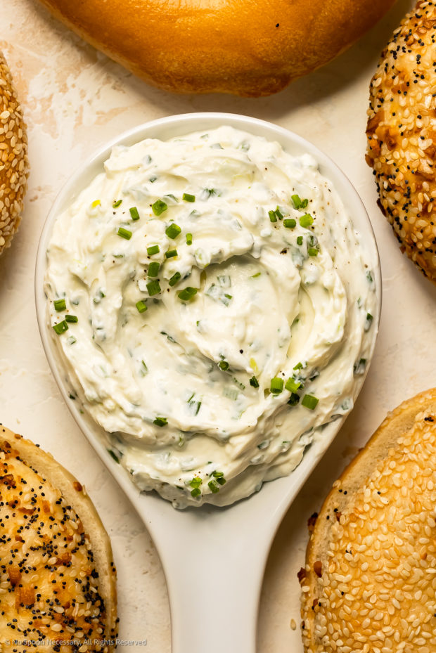 Overhead, close-up photo of flavored cream cheese with chives in a white bowl.