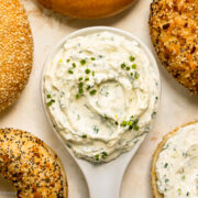 Overhead photo of whipped cream cheese in a small bowl with bagels surrounding the cream cheese.
