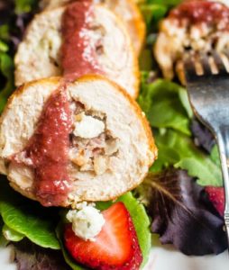 Straight on, up-close shot of a Chicken Roulade stuffed with Gorgonzola, Bacon & Caramelized Onions and drizzled with a Strawberry Balsamic Reduction on a plate of mixed greens.