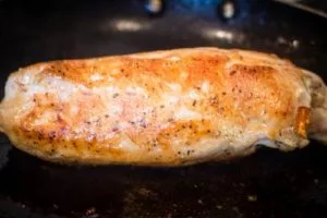 Angled shot of a chicken roulade being browned in a skillet.