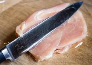 Angled shot of a knife slicing open a chicken breast for stuffing for a chicken roulade.