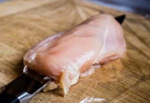 Angled shot of a chef knife slicing open a chicken breast for stuffing for a chicken roulade.