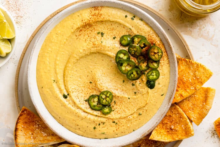 Overhead photo of jalapeno dip with cream cheese in a white bowl with pita chips next to the bowl.