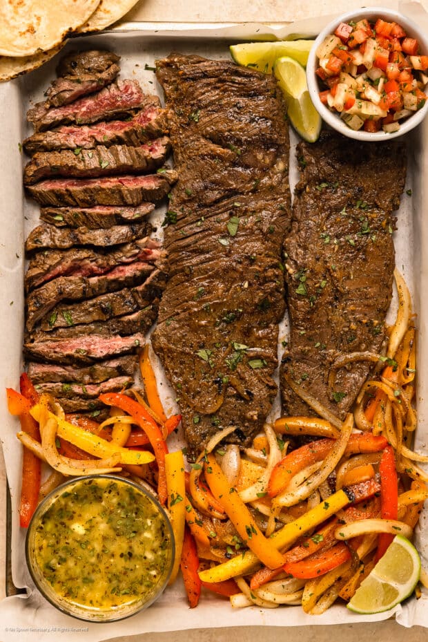 Photo of grilled skirt steak, peppers, onions and tortilla on a serving tray.