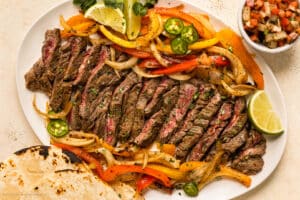 Overhead photo skirt steak fajitas with peppers, onions, and tortillas on a serving platter.