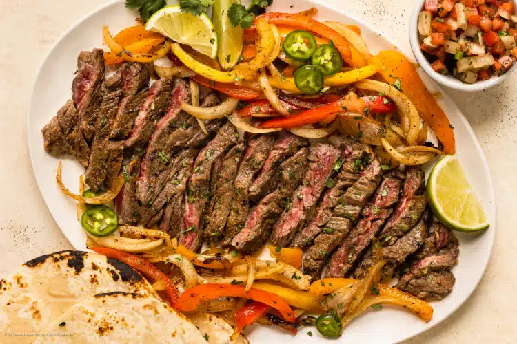 Overhead photo skirt steak fajitas with peppers, onions, and tortillas on a serving platter.