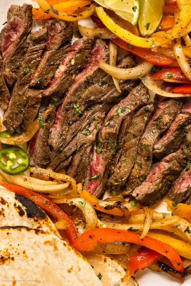 Overhead photo of grilled skirt steak with peppers and onions for fajitas recipe.