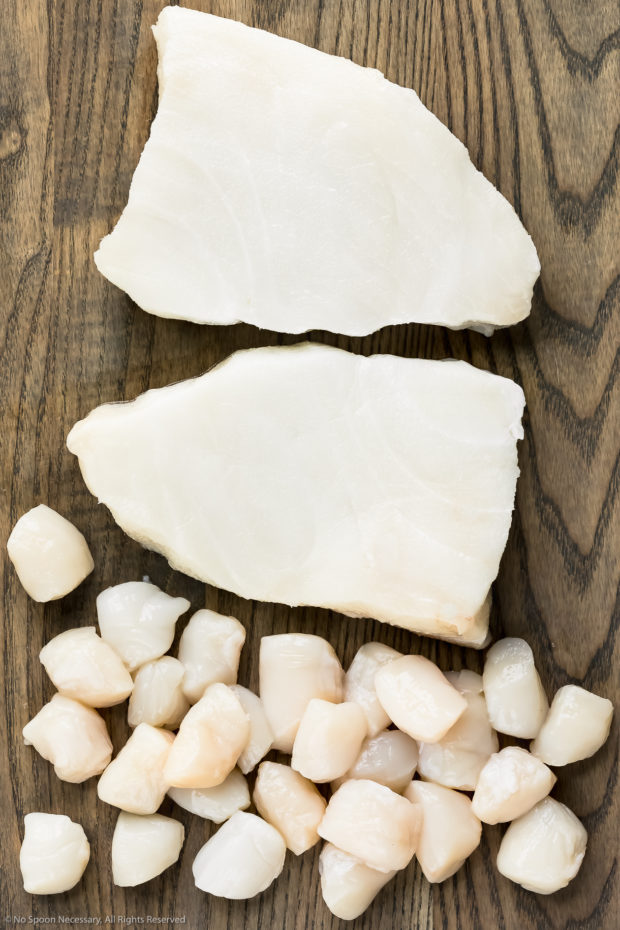 Overhead photo of filets of semi-firm white fish and bay scallops on a cutting board - photo of the two main ingredients in ceviche.