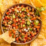 Overhead photo of a bowl of easy pico de gallo with a tortilla chip inserted into the dip.