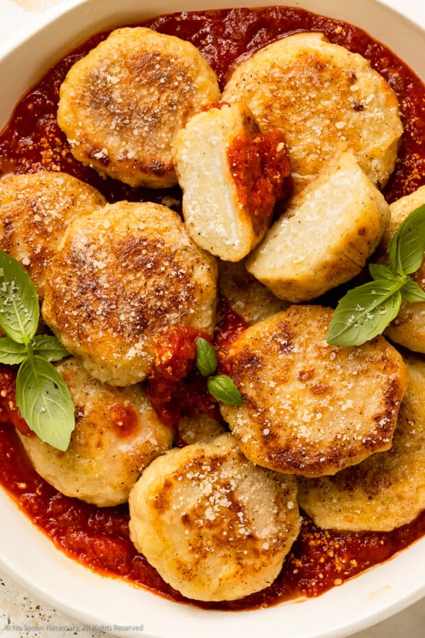 Overhead photo of a bowl of ricotta gnocchi in marinara sauce with basil.
