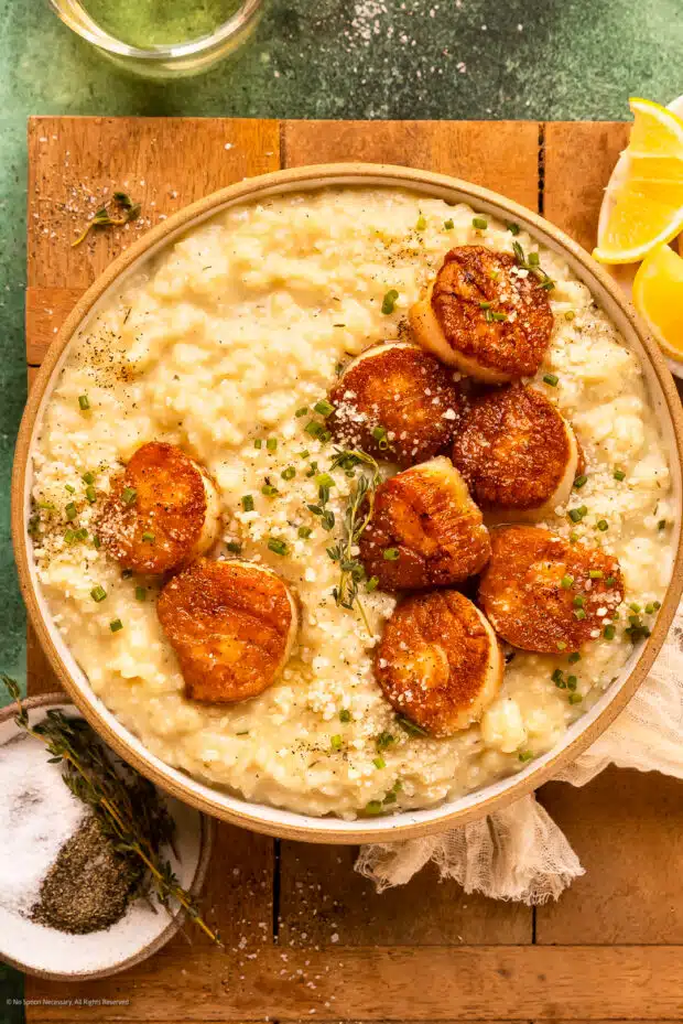Overhead photo of seared scallops over risotto with fresh herbs in a white serving bowl.
