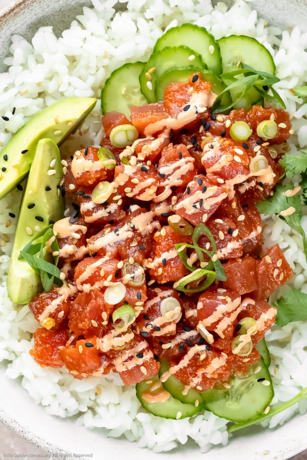 Overhead, close-up photo of Homemade Spicy Tuna Sushi Bowl drizzled with spicy mayonnaise and garnished with slices of avocado, cucumber, scallions and fresh cilantro. 