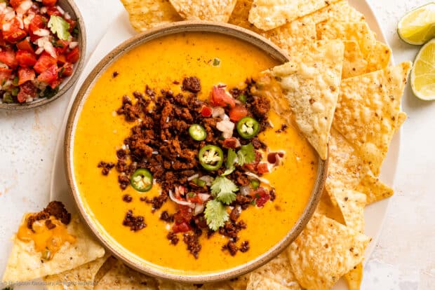 Overhead photo of chile con queso with ground meat in a serving bowl with tortilla chips scattered around the bowl.