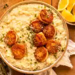 Overhead photo of risotto scallops garnished with parmesan cheese and fresh herbs in a white serving bowl.