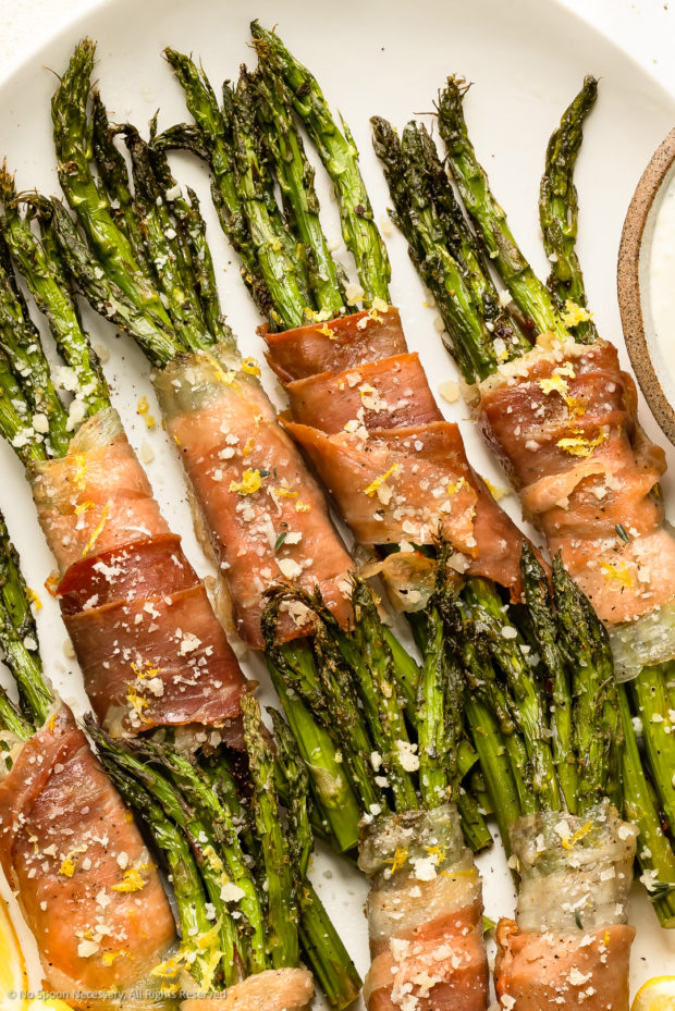 Overhead photo of roasted asparagus and prosciutto bundles on a white platter. 