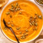 Overhead photo of roasted butternut squash soup garnished with pumpkin seeds and honey in a white bowl.