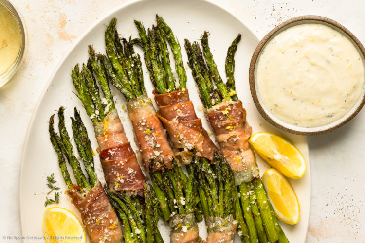 Overhead photo of prosciutto wrapped asparagus with creamy asparagus sauce on a white platter.