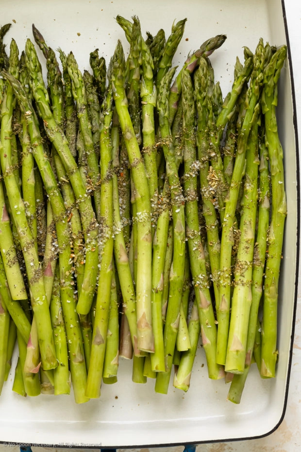 Overhead photo of raw asparagus spears sprinkled with seasonings.