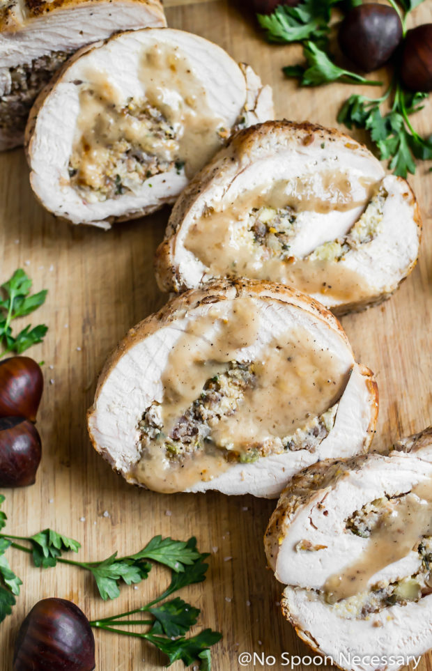Angled overhead shot of a sliced Thanksgiving Turkey Breast Roulade with Stuffing drizzled with gravy on a cutting board with chestnuts and fresh parsley surrounding the roulade.