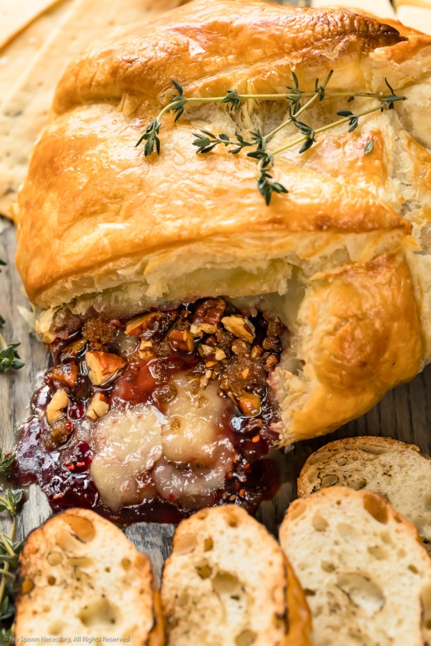 Angled, up close photo of Baked Brie en Croute that has been cut into to showcase the oozing cheese, jam and nuts. 