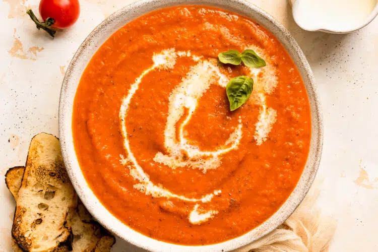 Overhead photo of tomato soup homemade from scratch with fresh basil leaves in a white serving bowl.