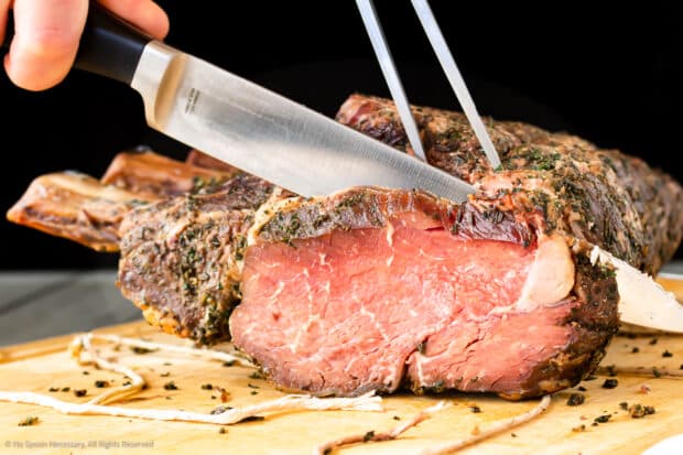 Action photo of a carving knife slicing a prime rib roast.