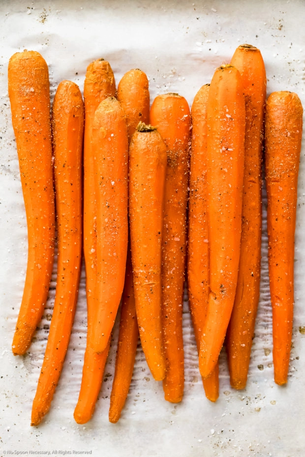 Overhead photo of roasted carrots seasoned with salt and pepper on a parchment paper lined sheet pan - photo of cooked carrots to make dip.