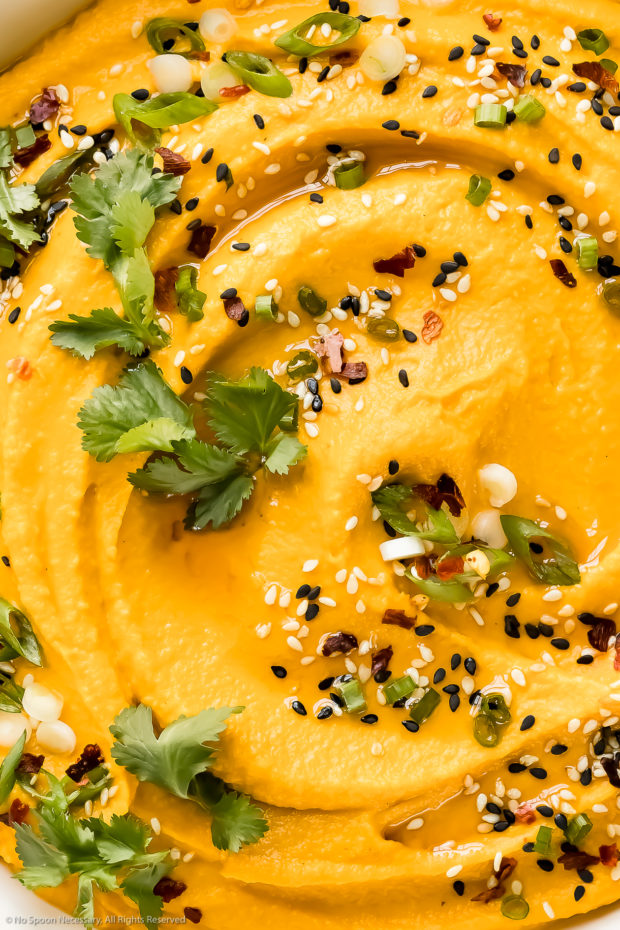Overhead, up close photo of creamy carrot dip garnished with fresh cilantro, sesame seeds and scallions.