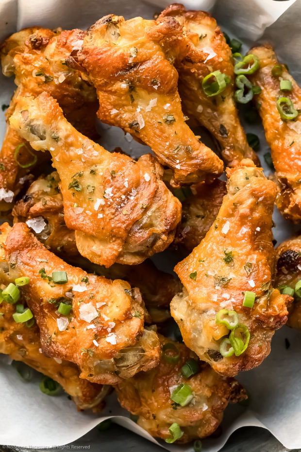 Overhead, upclose photo of baked salt and vinegar chicken wings garnished with flaky sea salt and sliced scallions.