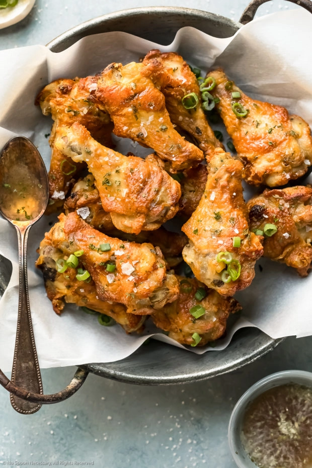 Overhead photo of Salt and Vinegar Wings in a metal serving bowl lined with parchment paper with a spoonful of vinegar dipping sauce resting on the side of the bowl.