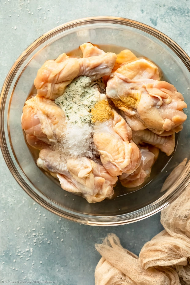 Overhead photo of raw chicken wings topped with the ingredients for salt and pepper marinade in a glass bowl - photo of step 2 of the recipe.