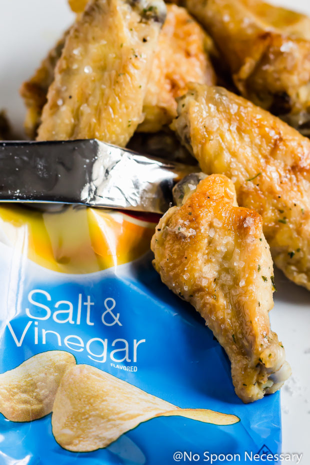 Slightly angled, overhead shot of Baked Salt & Vinegar Chicken Wings pouring out of a salt and vinegar chips bag.