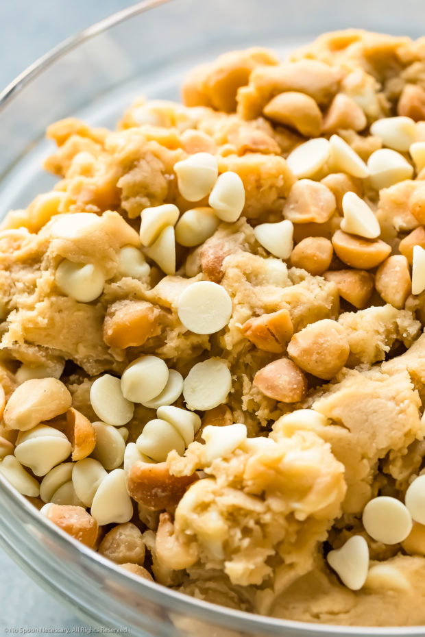 Angled up-close photo of white chocolate macadamia nut cookie dough in a glass bowl.