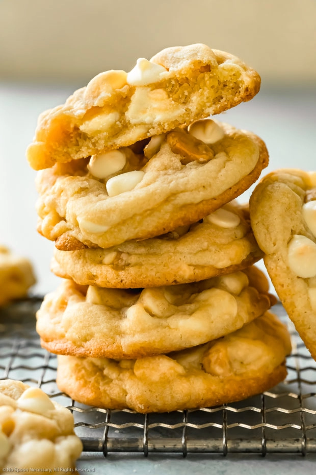 Straight on shot of a stack of white chocolate macadamia nut cookies on a wire rack with the top cookie torn in half to show the soft and chewy interior.