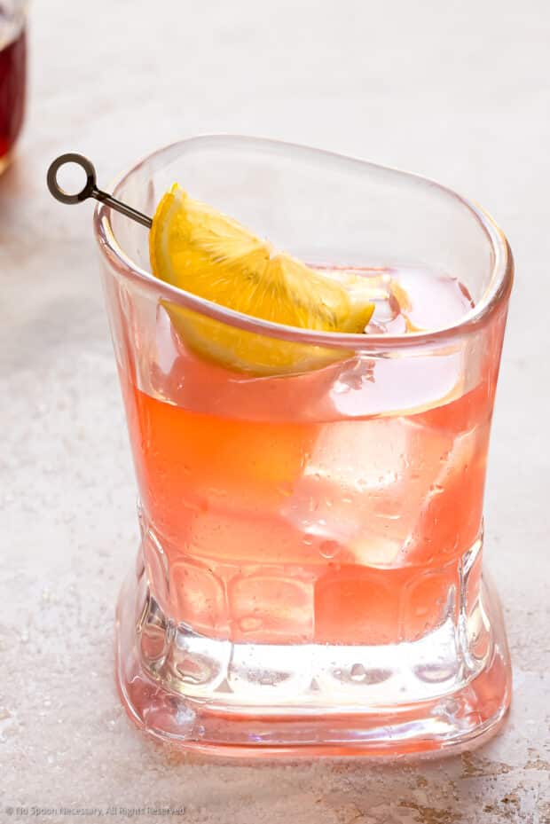 Straight on photo of a pink lemonade cocktail garnished with a lemon wedge.