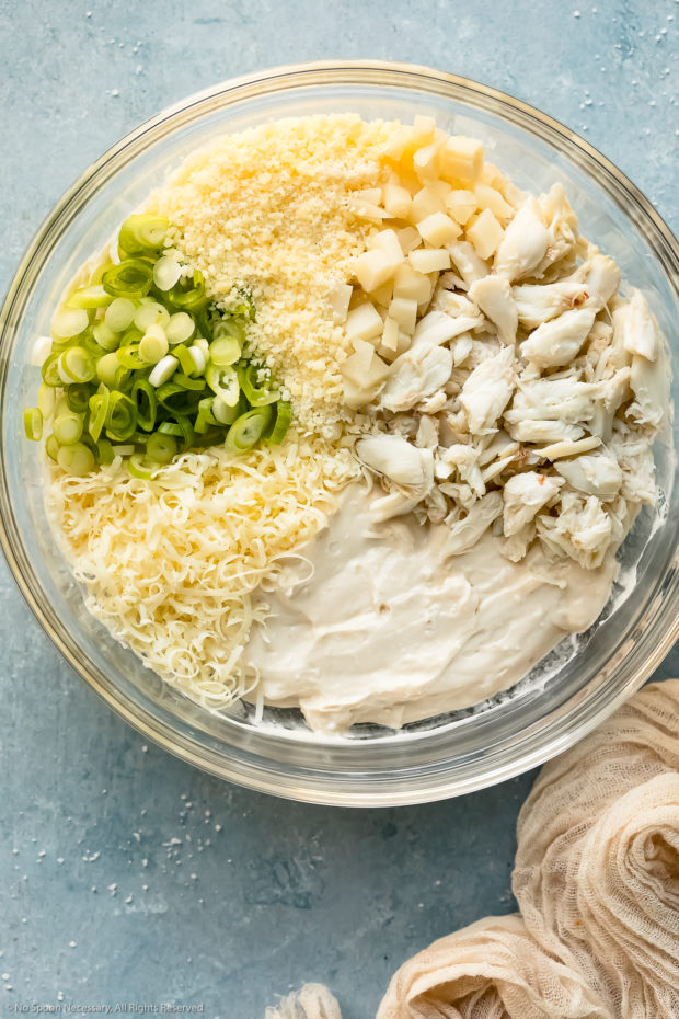 Overhead photo of all the ingredients needed to make lump crab dip neatly organized in a glass bowl before being stirred together.