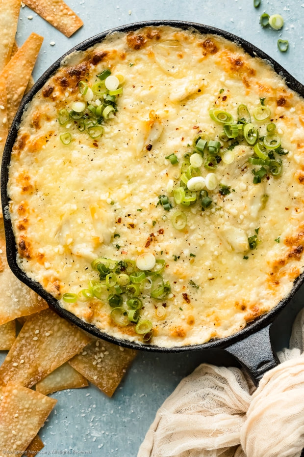 Overhead, close-up photo of Crab Rangoon Dip garnished with fresh scallions in a cast iron skillet with wonton chips scattered next to the skillet.
