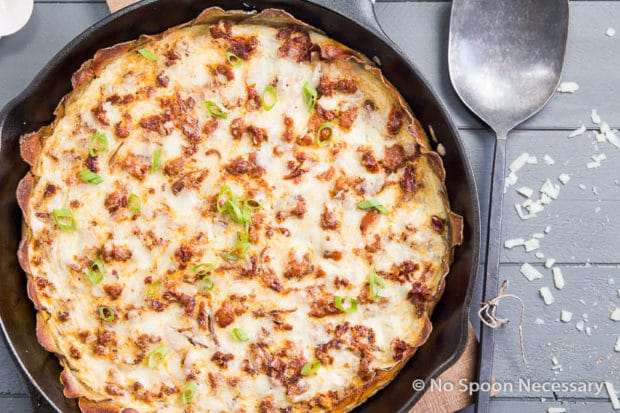 Overhead shot of Spanish Potato Crusted Frittata in a cast iron skillet on top of a wood board with a large serving spoon next to the skillet.