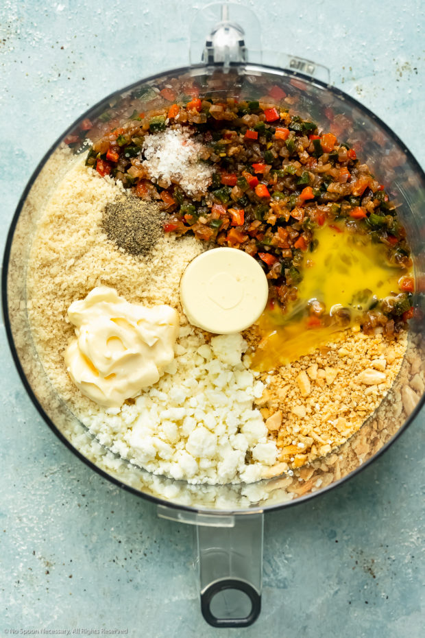 Overhead photo of a food processor bowl filled with the flavoring and binding ingredients needed to make black bean burger recipe.