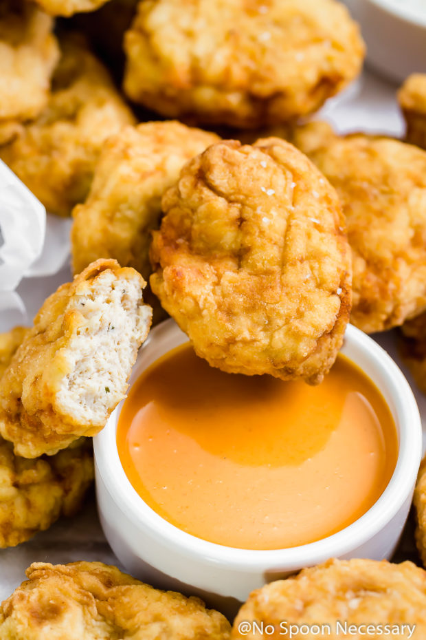 Overhead, up-close shot of Copycat McDonald's Buffalo Chicken Nuggets on a pile of more nuggets with a small ramekin of buffalo sauce under the nugget.