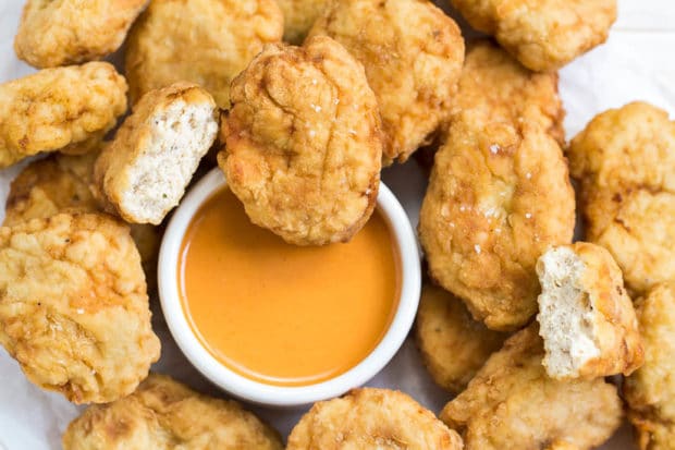 Overhead, up close shot of a pile of Copycat McDonald's Buffalo Chicken Nuggets on a piece of parchment paper with a small ramekin of buffalo sauce in the middle and a nugget barely dipped in.