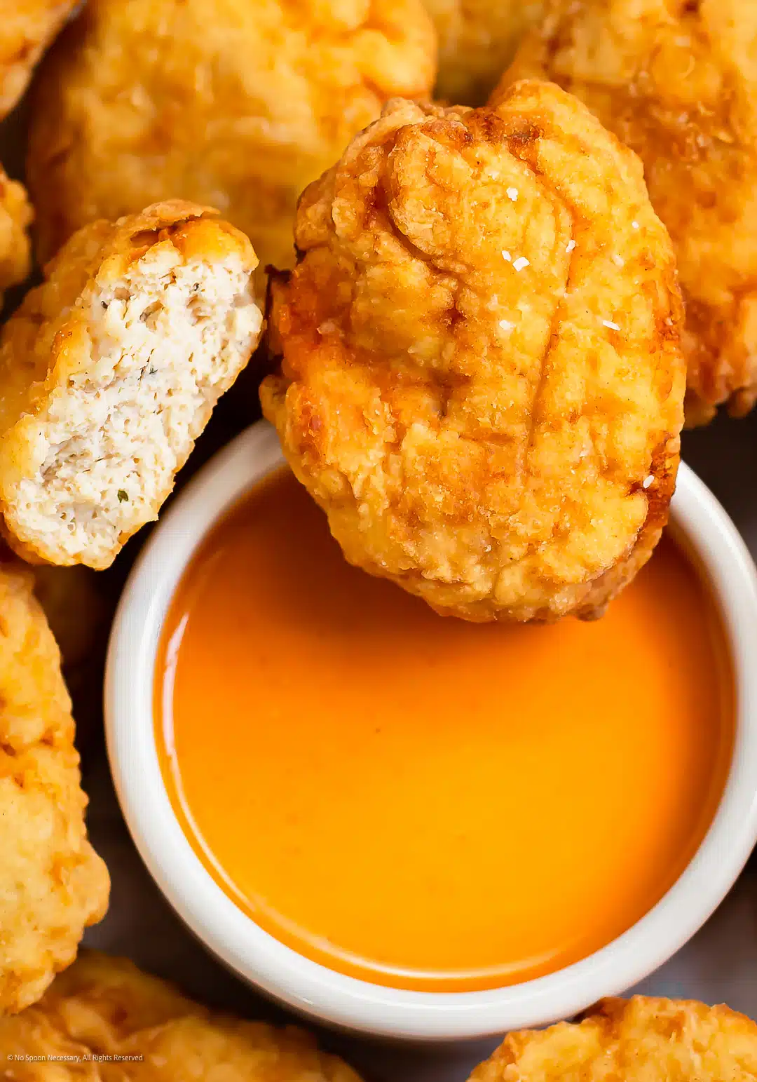 Close up photo of a McDonalds chicken nugget dunked into buffalo sauce.