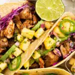 Overhead photo of two pork carnitas tacos with pineapple salsa and cabbage.