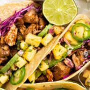 Overhead photo of two pork carnitas tacos with pineapple salsa and cabbage.