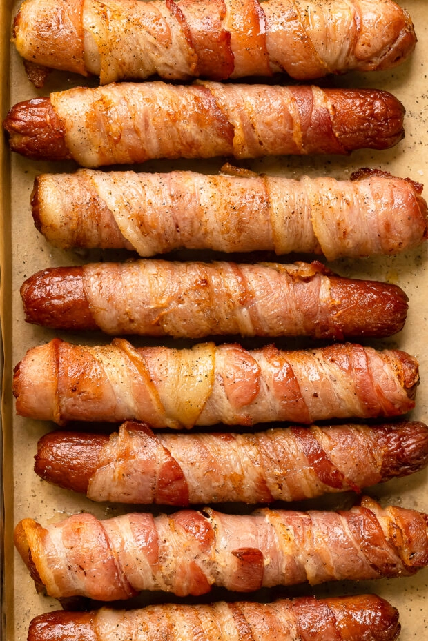 Overhead close-up photo of danger dogs (hot dogs wrapped in bacon) on a brown parchment paper. 