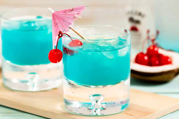 Photo of two Hawaiian Blue cocktails garnished with cherries and drink umbrellas.