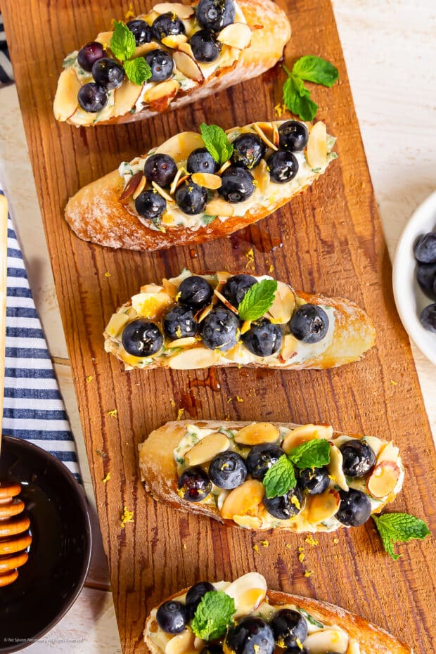 Overhead photo of five slices of blueberry ricotta toast on a wood serving trey. 