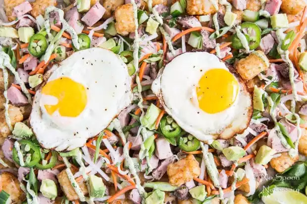Extreme up-close, overhead shot of Banh Mi Totchos (tater tot nachos) drizzled with cilantro-lime aioli and topped with two fried eggs.