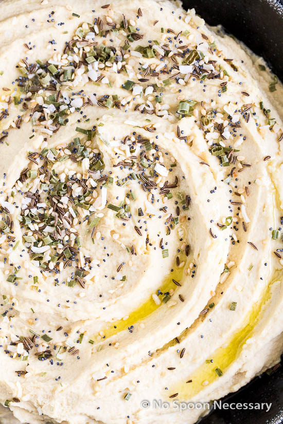 Overhead, upclose shot of a black bowl filled with Everything Bagel Hummus before being topped with lox.