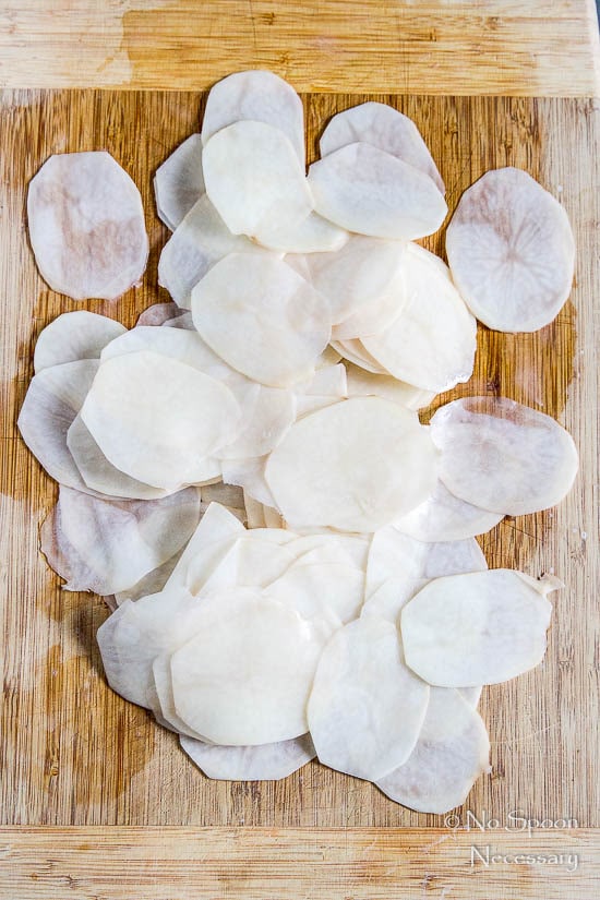 thinly sliced potatoes on a wooden cutting board